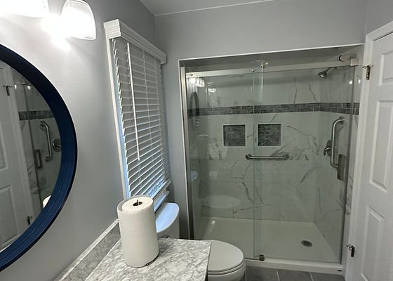 Remodeled bathroom with a sliding glass shower, marble-look walls and a navy round mirror